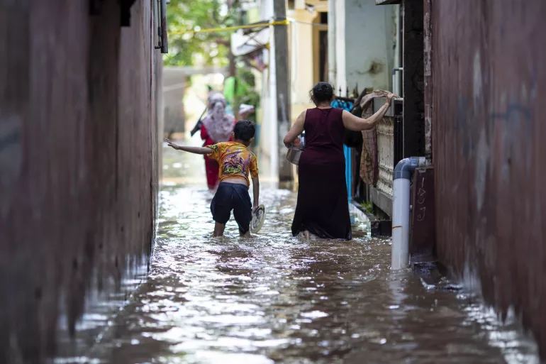 Em 21 de fevereiro de 2021, um menino e sua mãe caminham através das águas em uma área afetada por enchentes no leste de Jacarta, Indonésia.